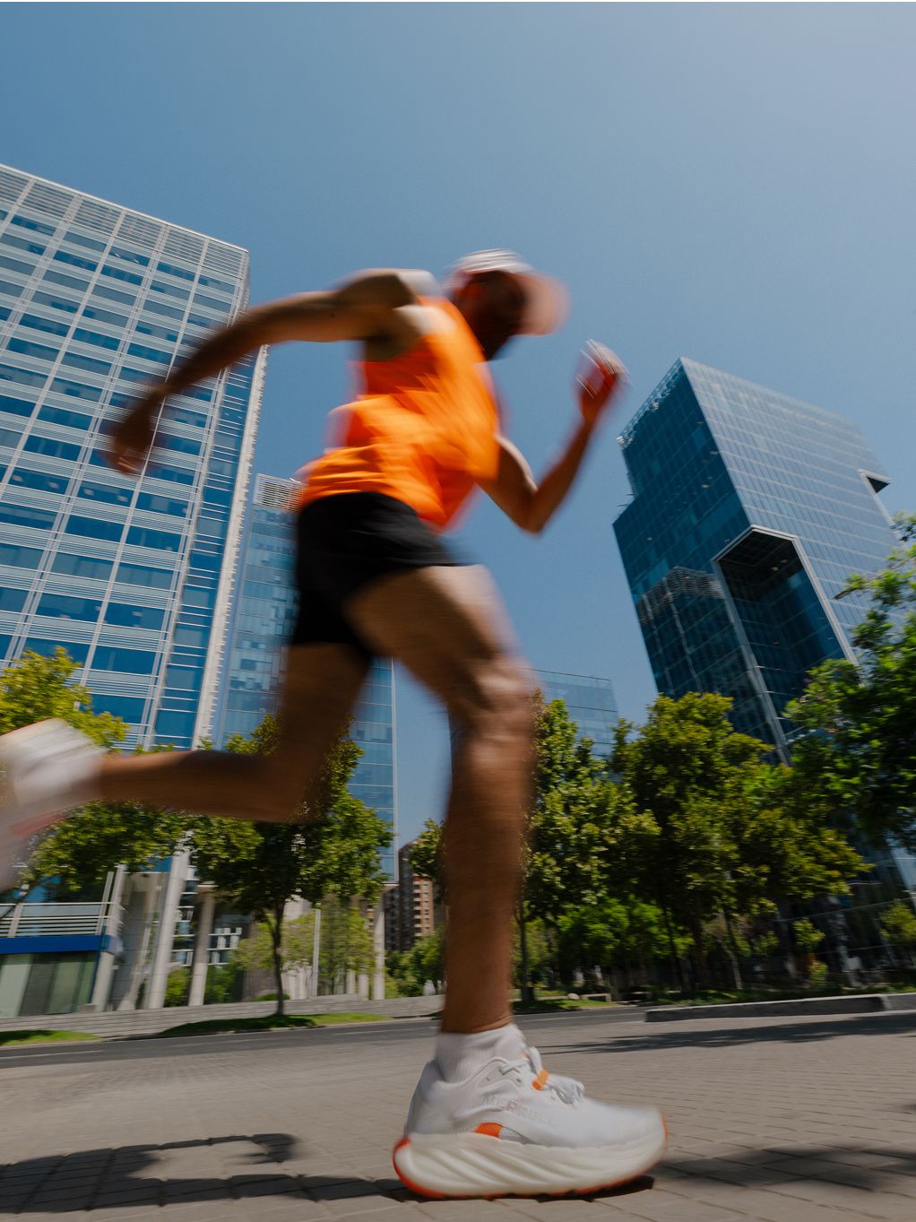 Person running in orange shirt past tall buildings wearing Merrell ProMorph shoes.